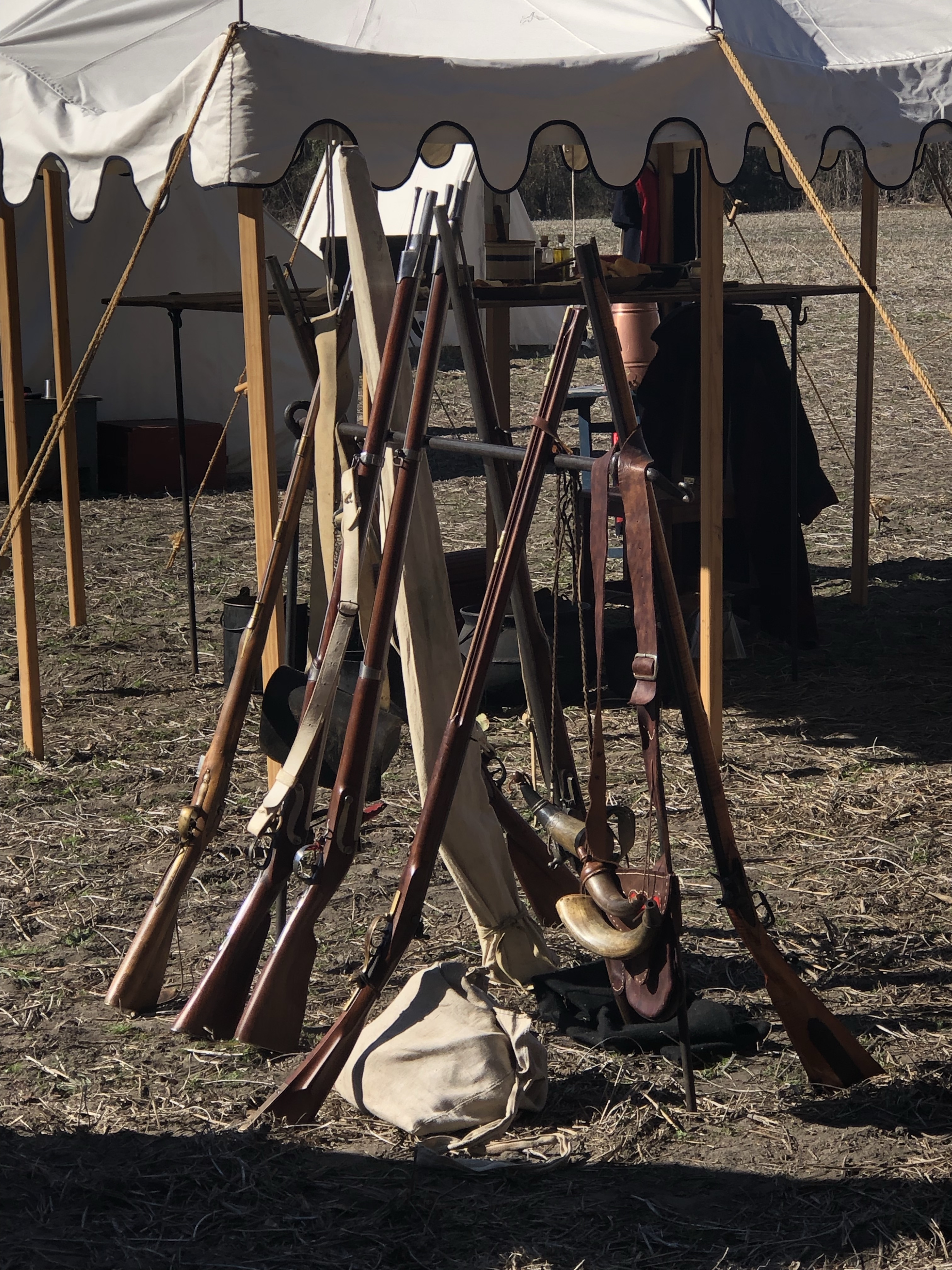 Muskets stacked against a rack in front of a tent