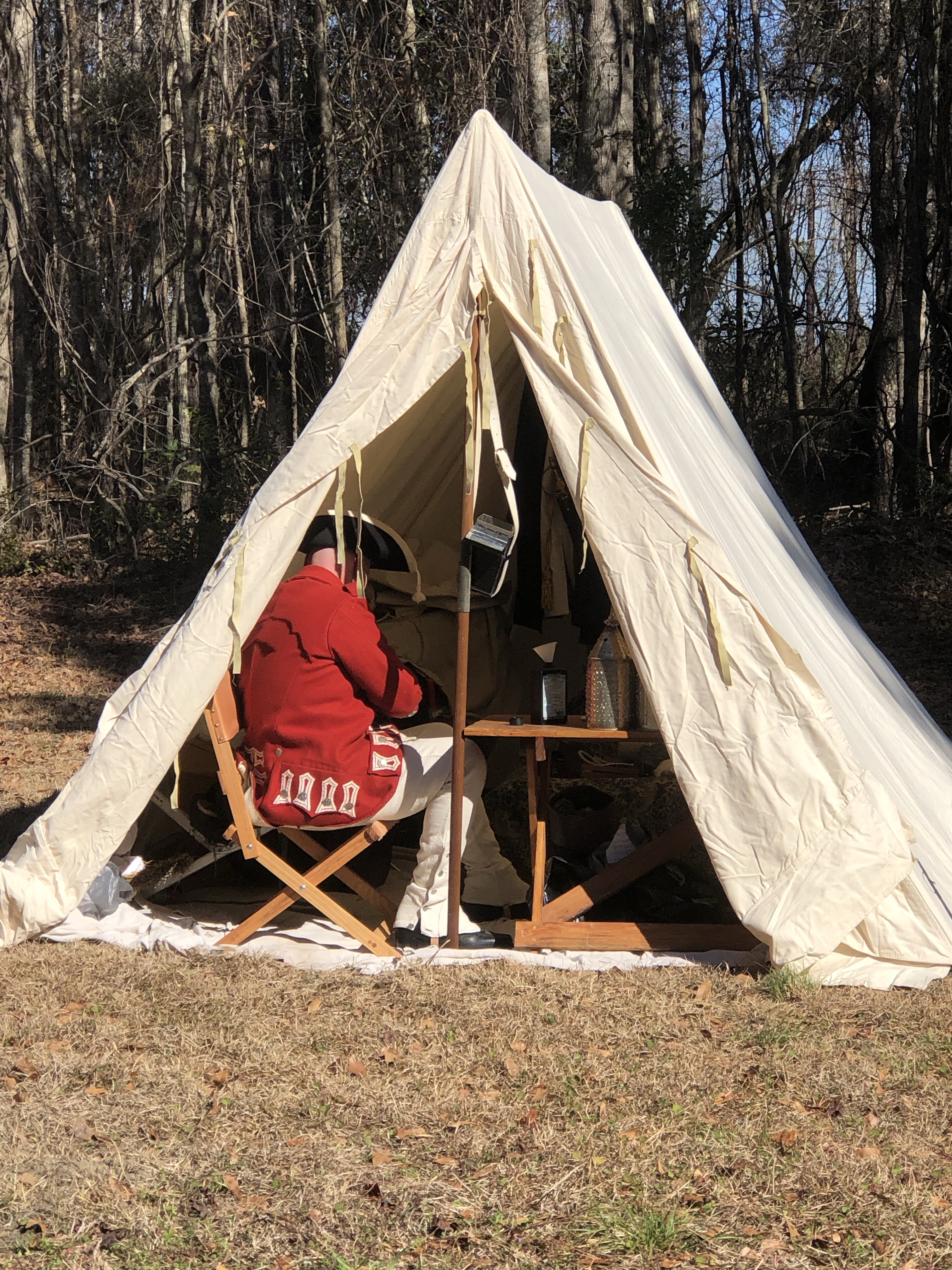 Reenactor seated in a red coat inside an open tent