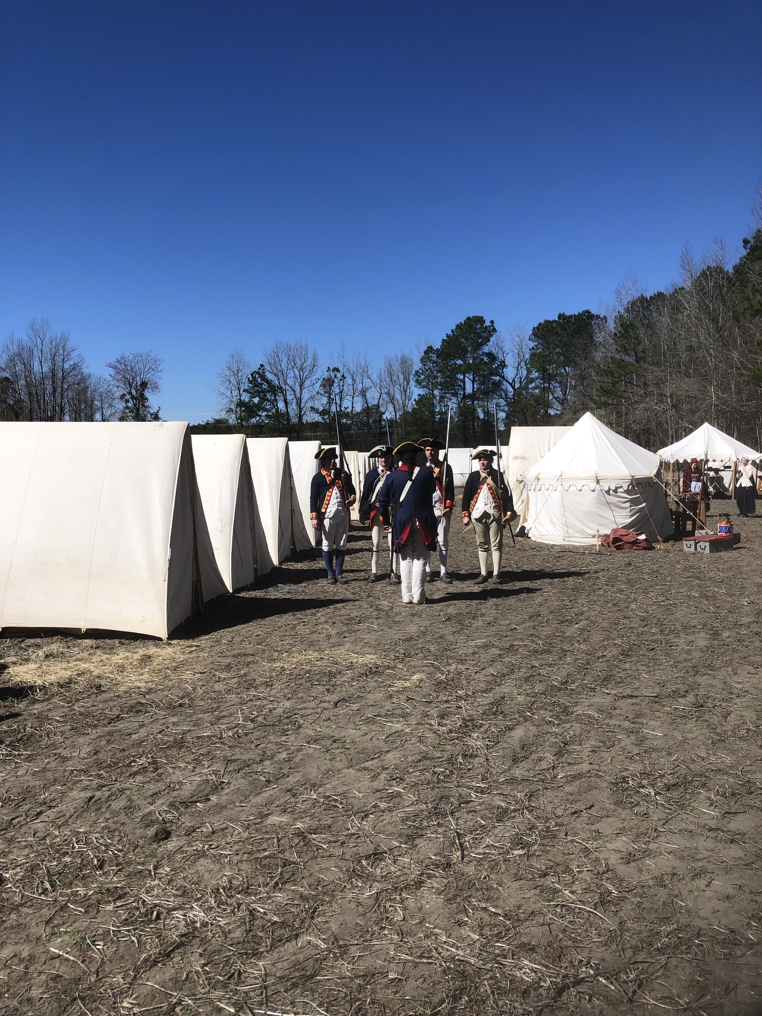 Reenactors in uniform walking past a row of tents