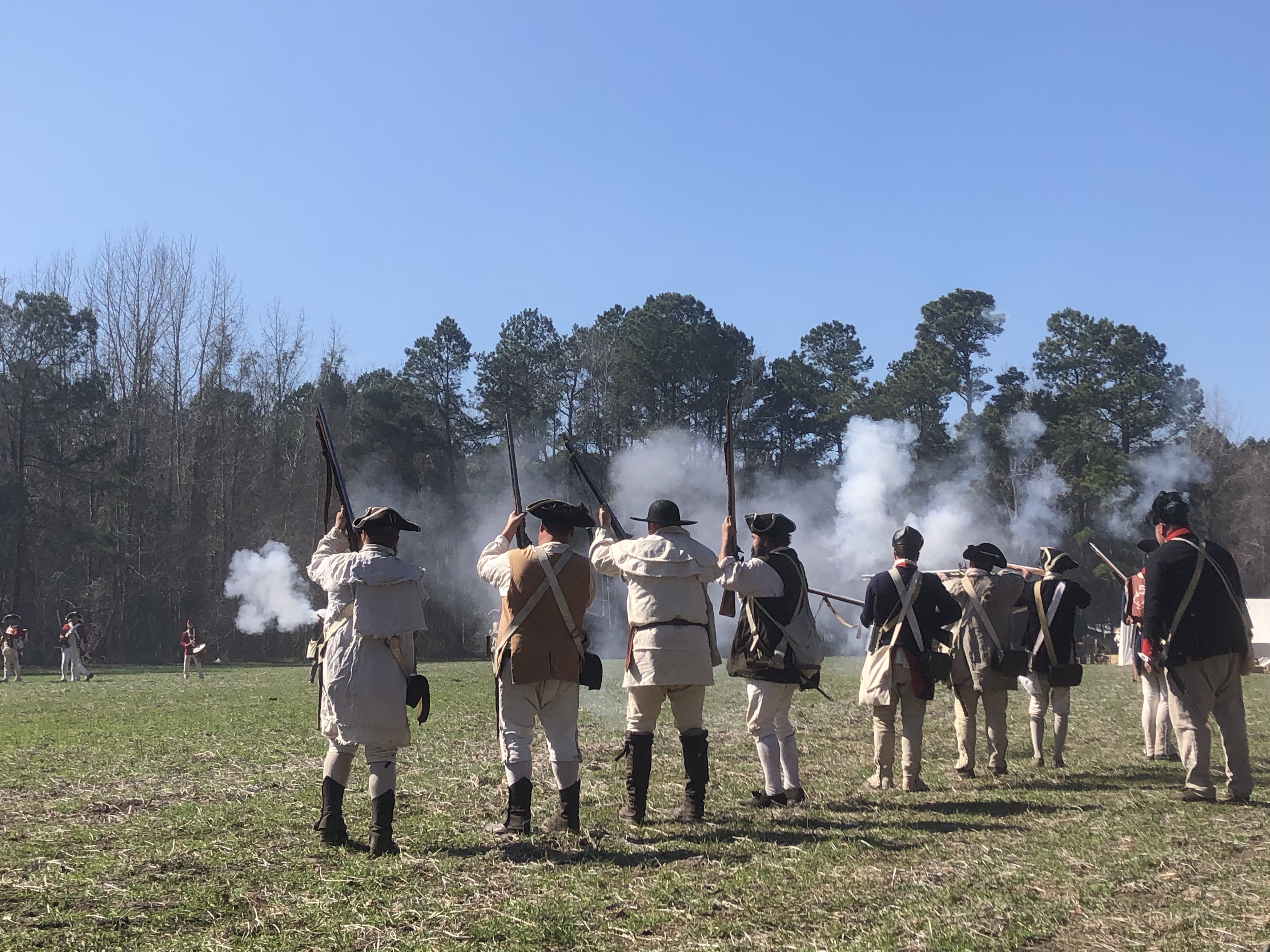 Reenactors firing a volley across the field