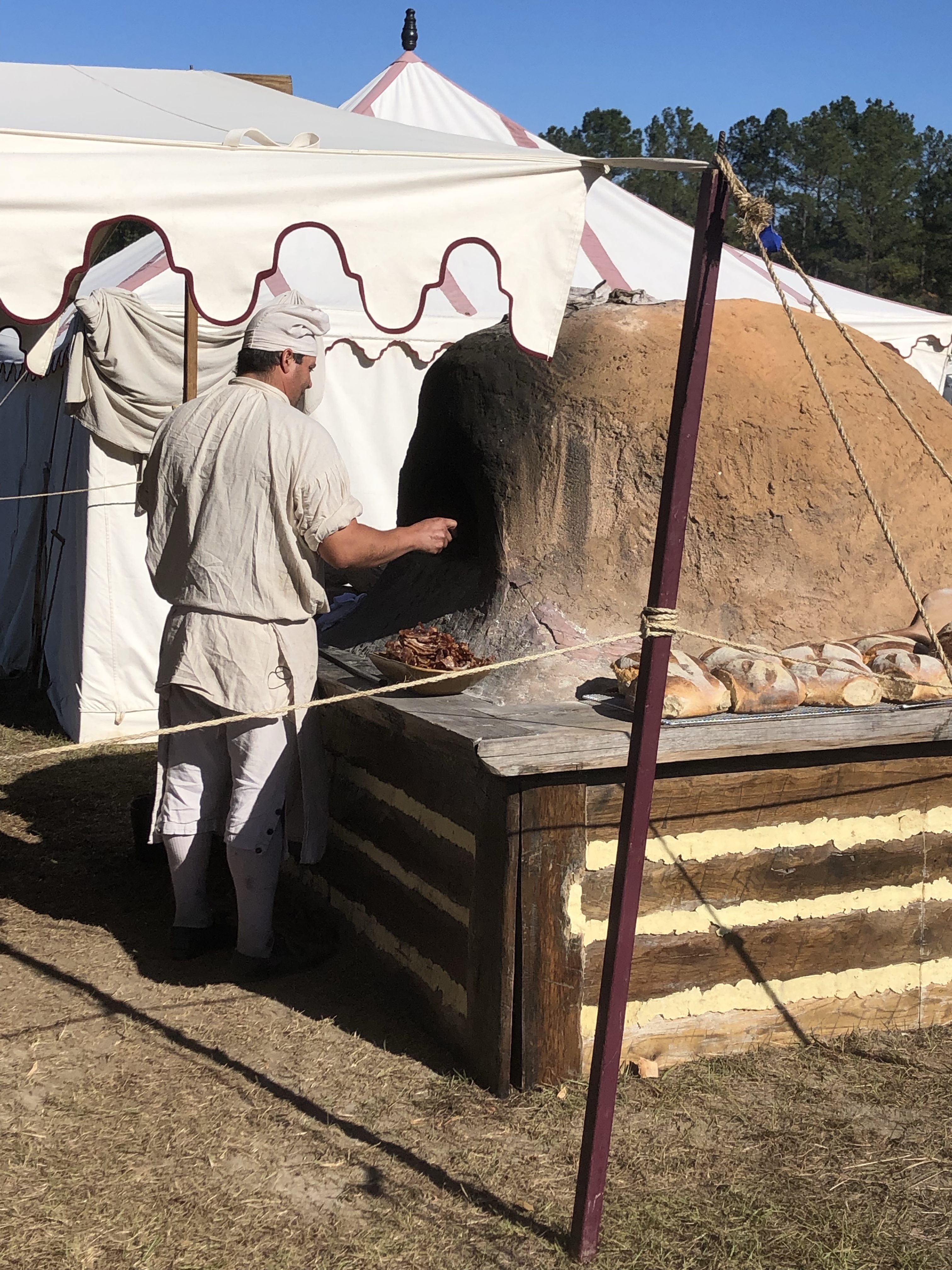 Reenactor baking bread in a domed clay oven at the camp