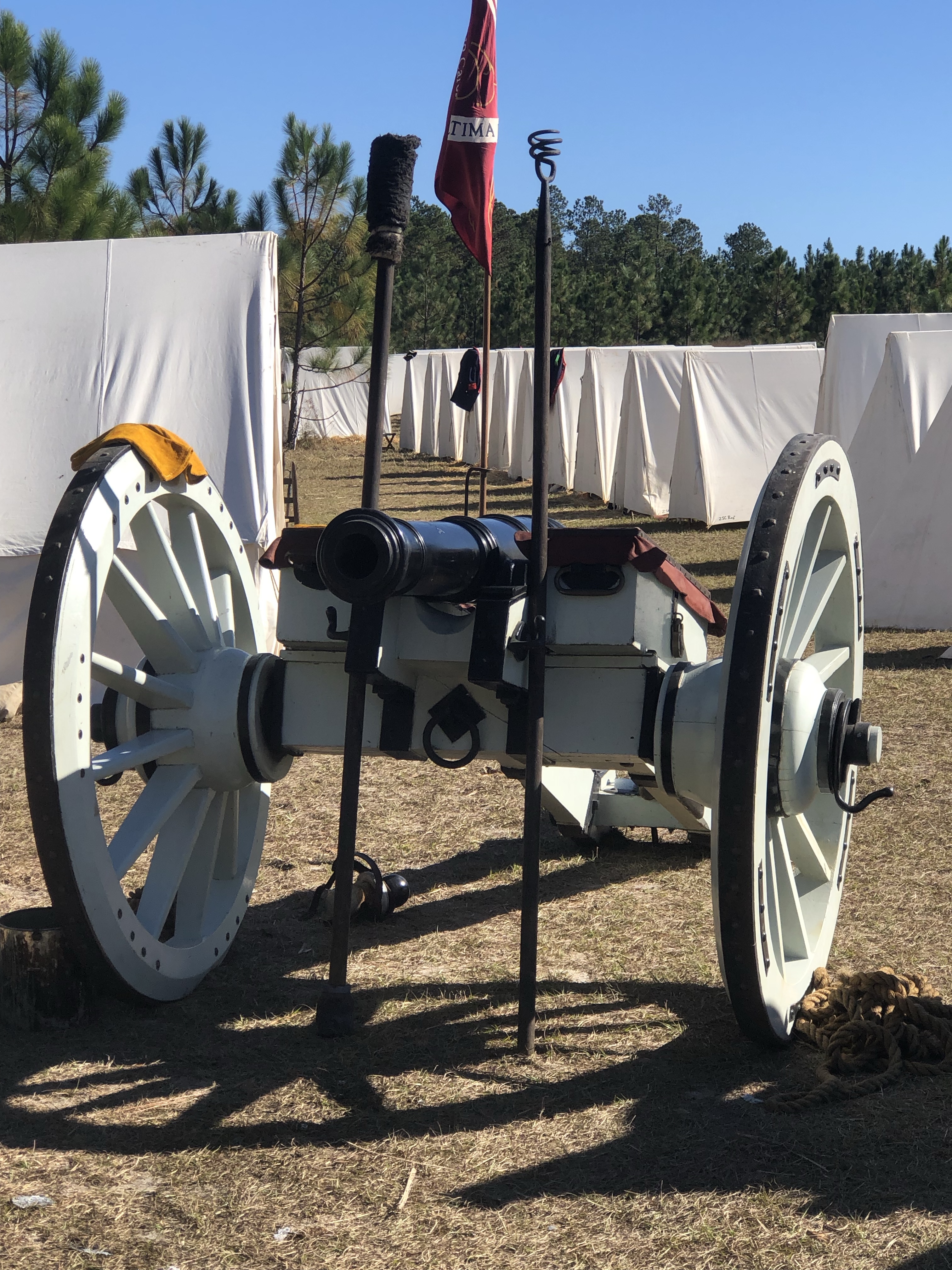 Close view of a field cannon on its carriage with a red flag and tents behind