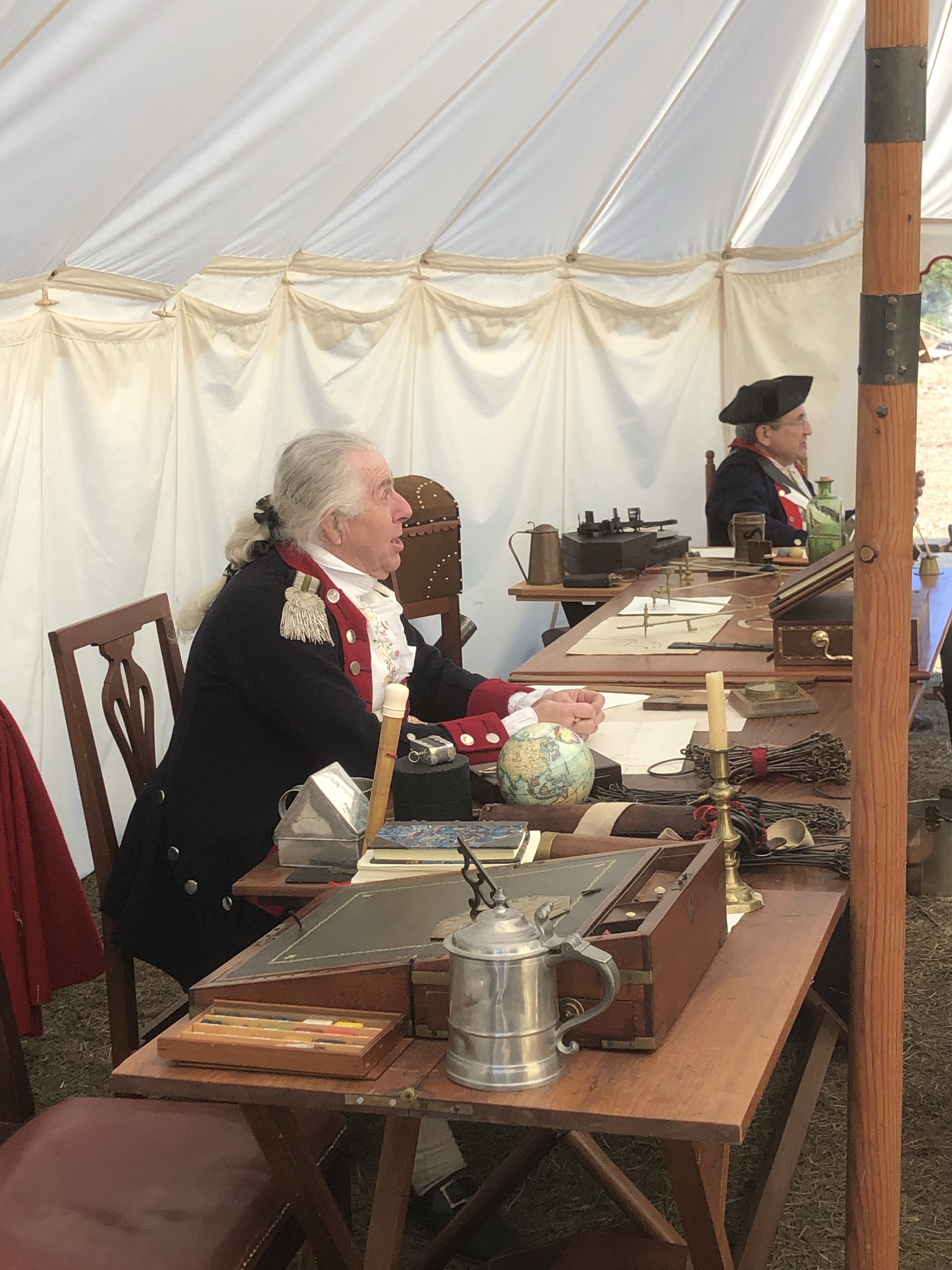 Reenactors in uniform seated at a table in a tent, demonstrating mapmaking and surveying
