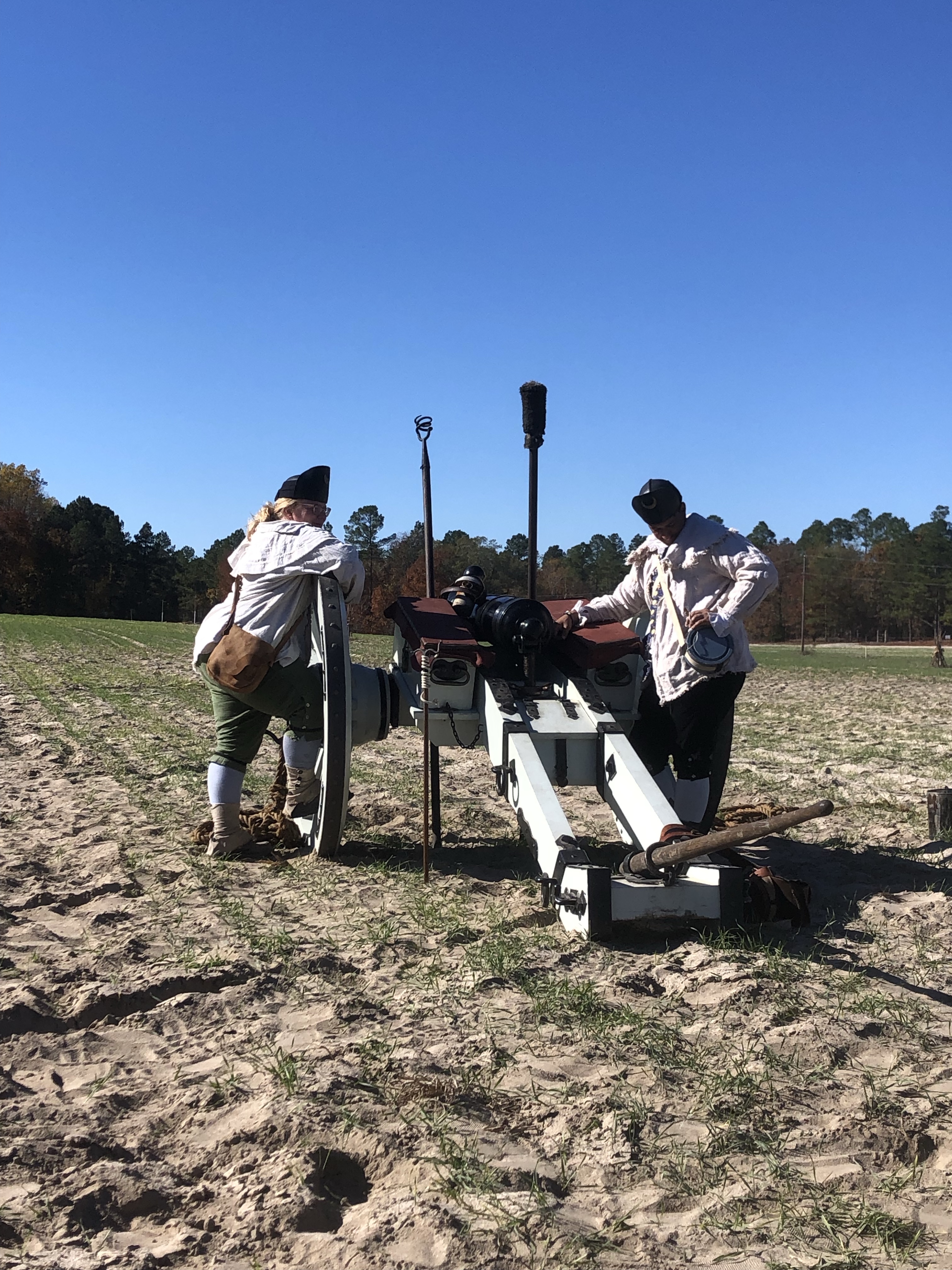 Two reenactors in hunting shirts tending a field cannon
