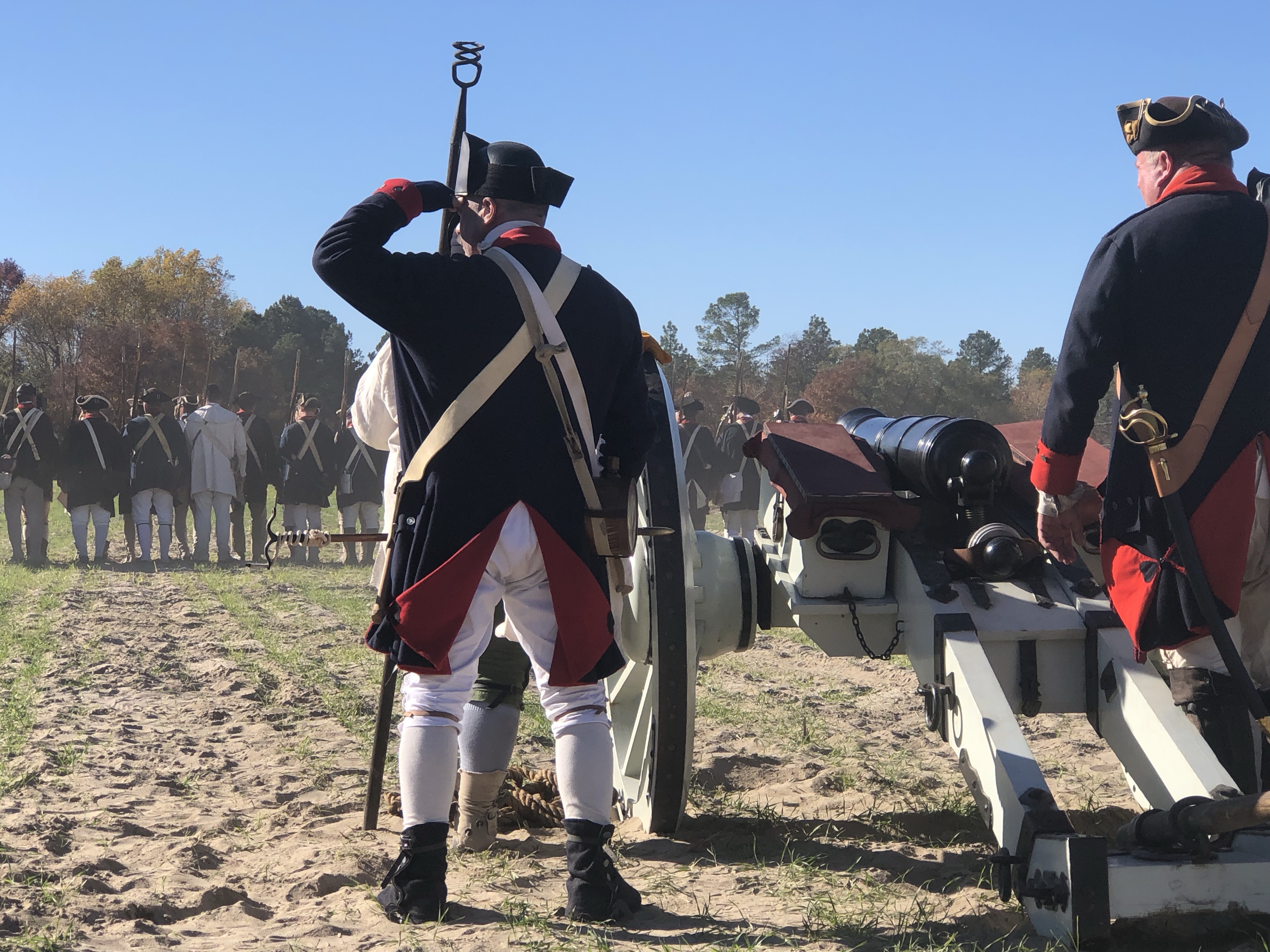Reenactors in blue Continental coats beside a cannon, one shading his eyes
