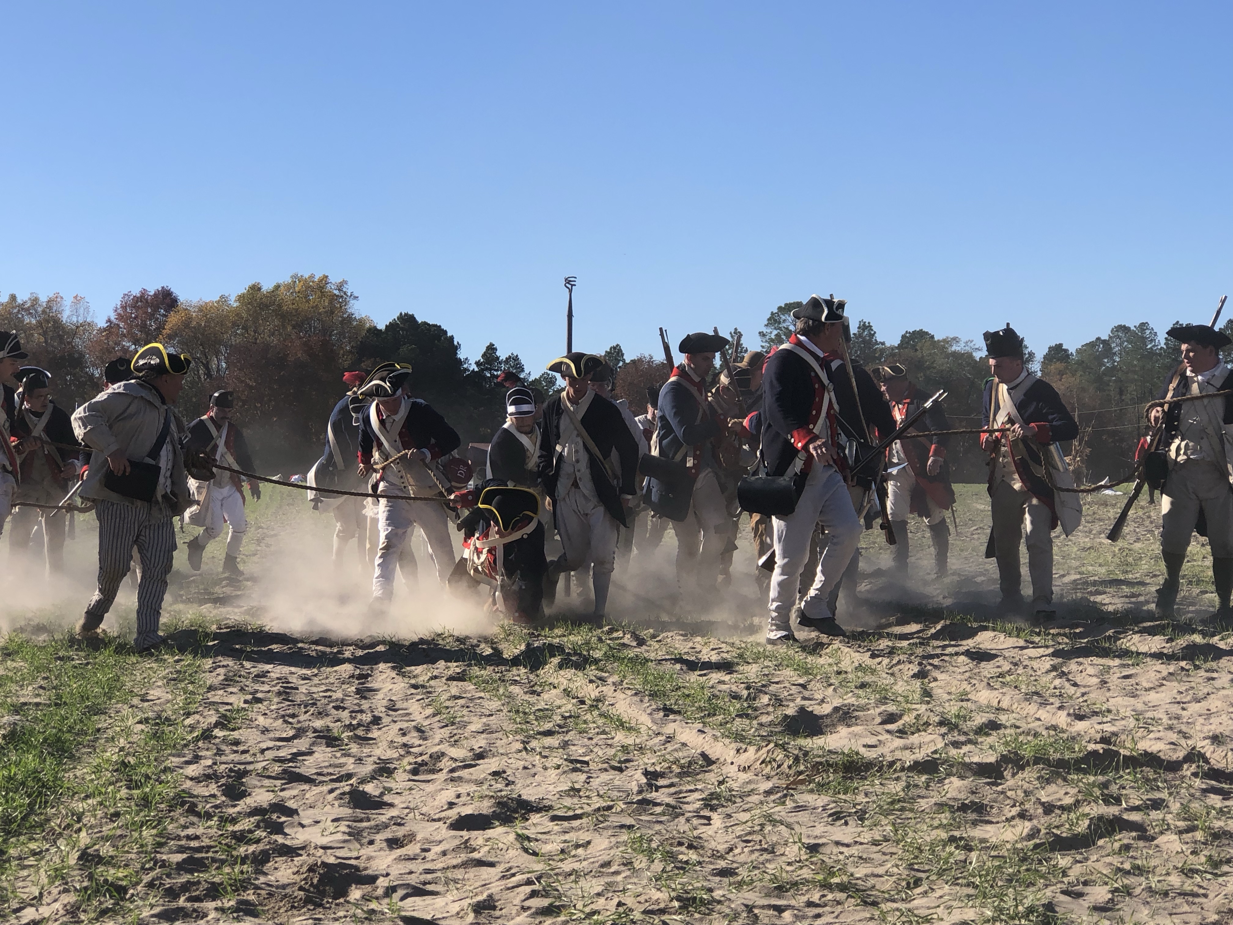 Line of infantry reenactors advancing through dust on the field