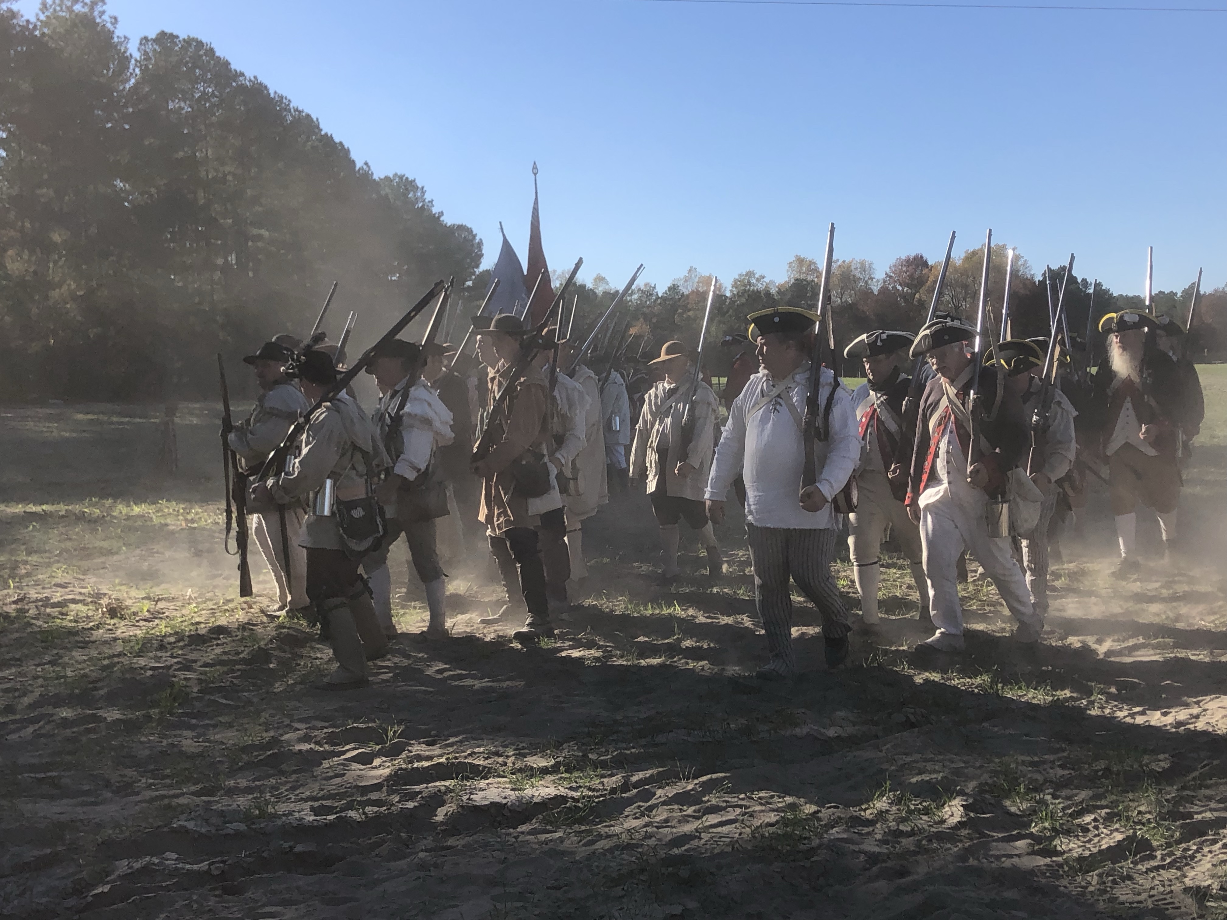 Militia reenactors with shouldered muskets moving through dust