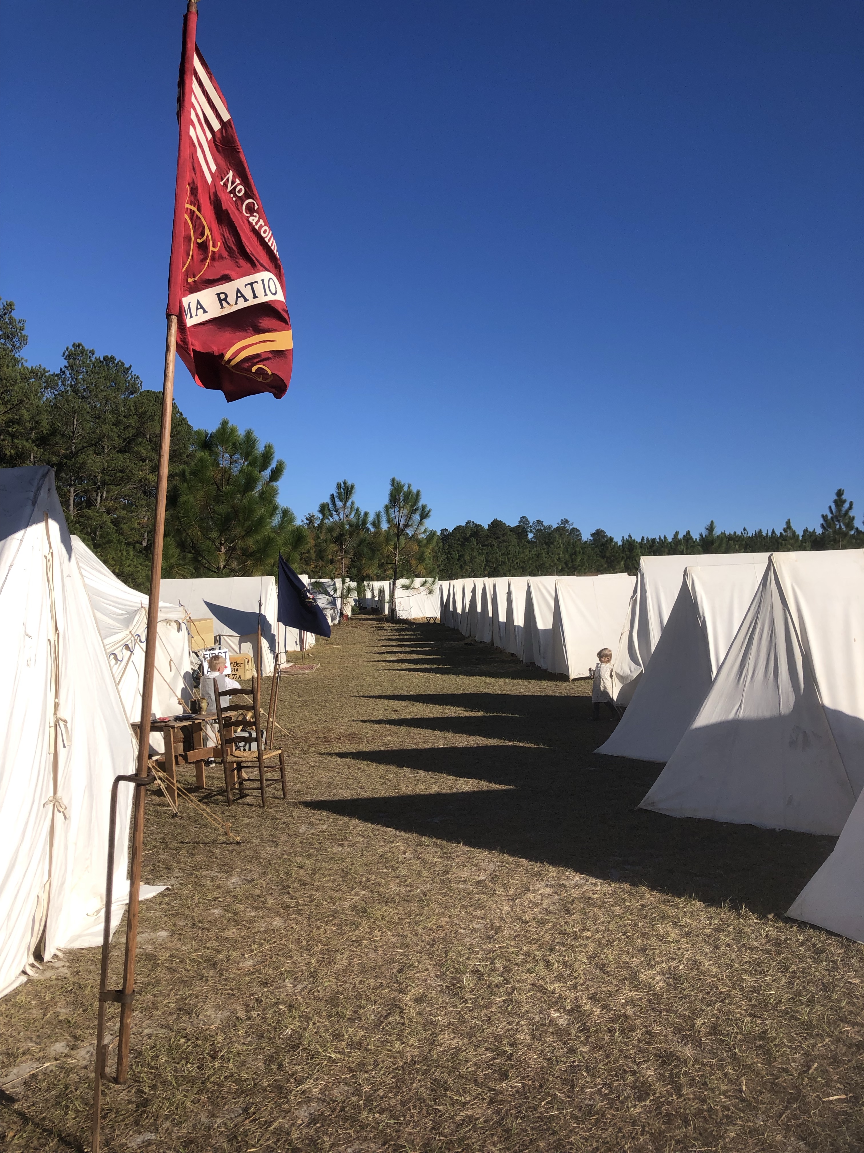 Rows of white canvas tents and a red regimental flag at the reenactment camp
