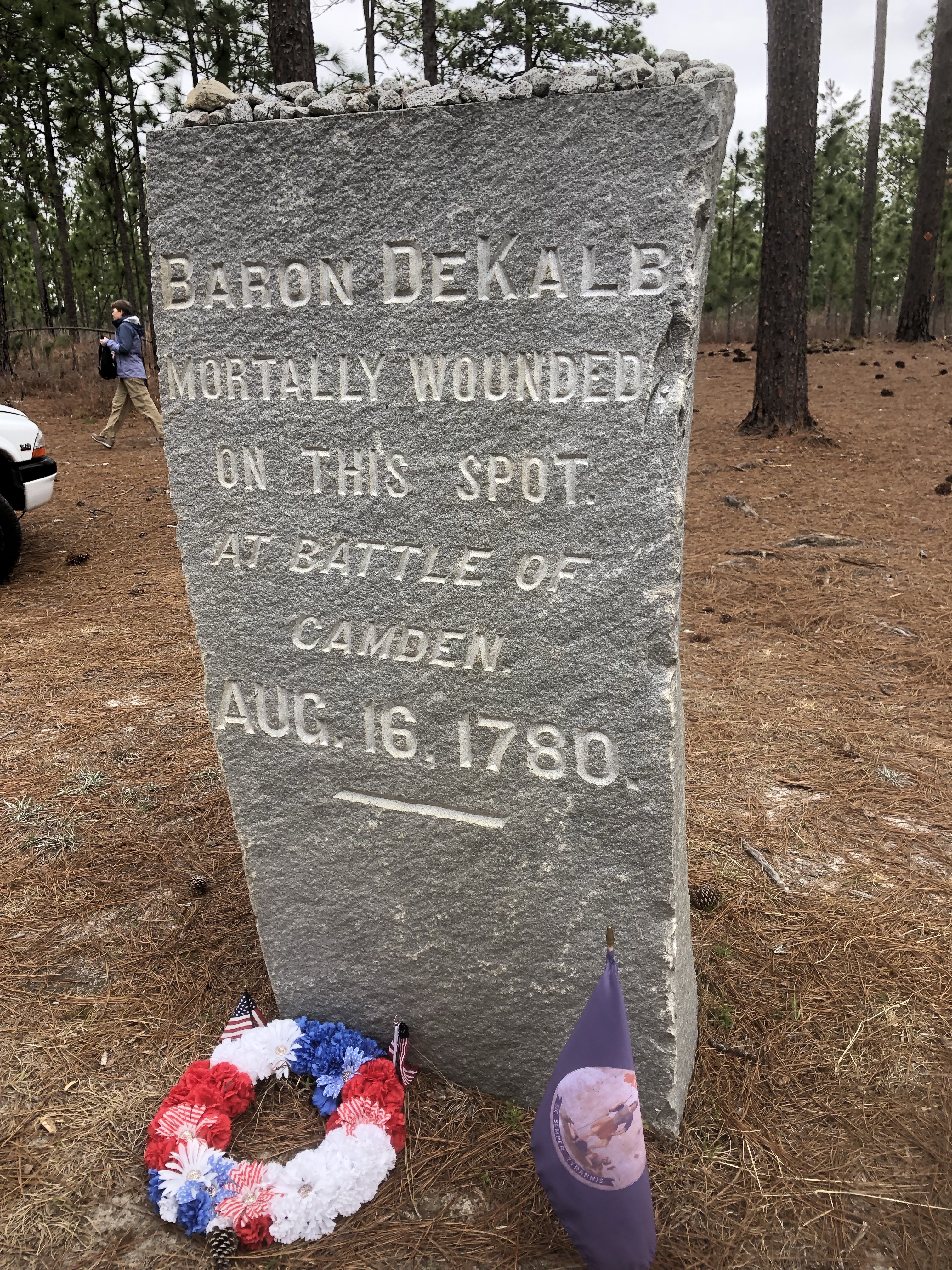Close view of the granite Baron DeKalb marker on the Camden battlefield, with a wreath and flag