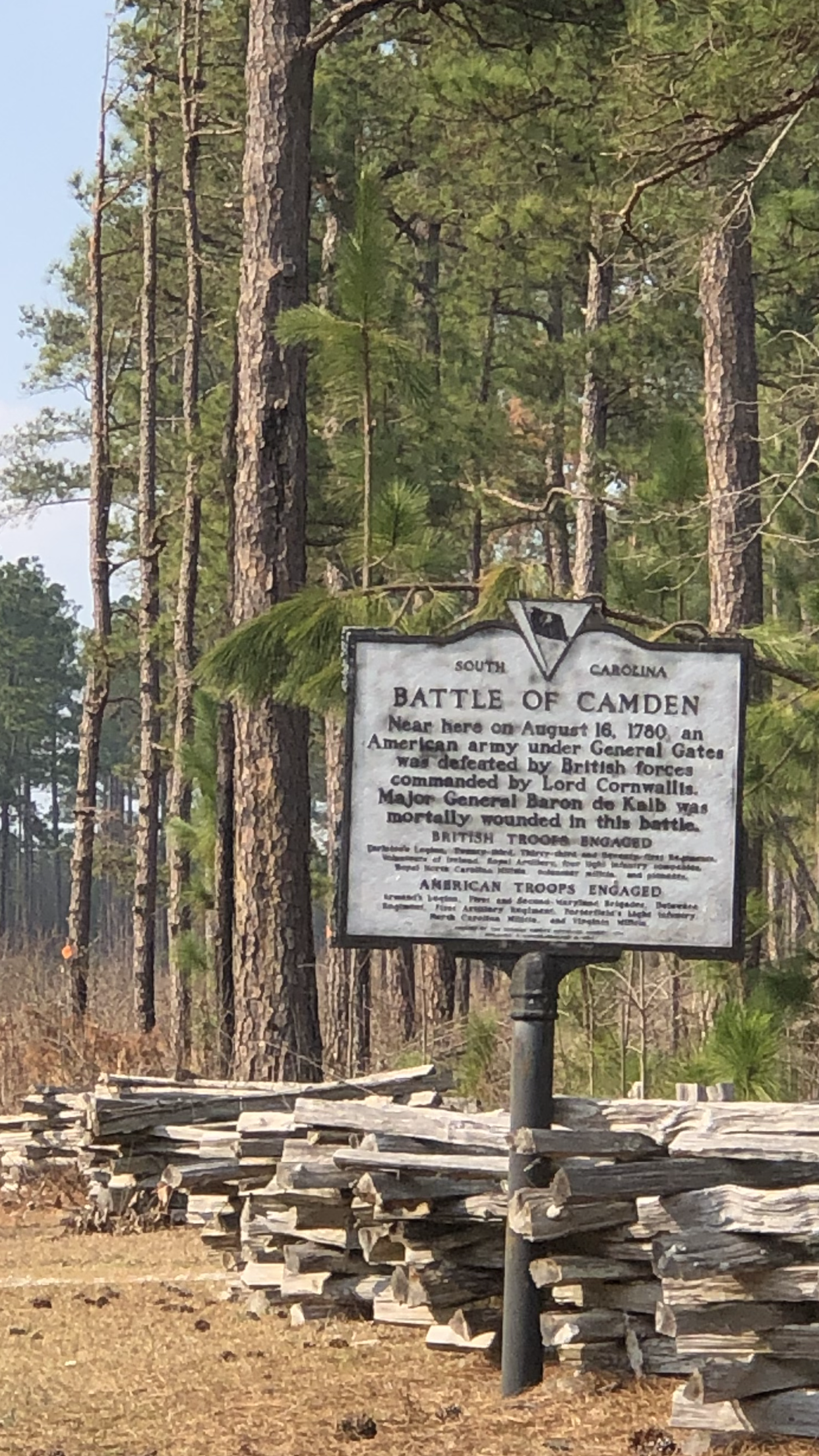 Battle of Camden historical marker beside a split-rail fence in the pines