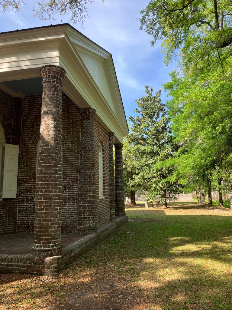 Brick portico columns and pediment with oaks beyond