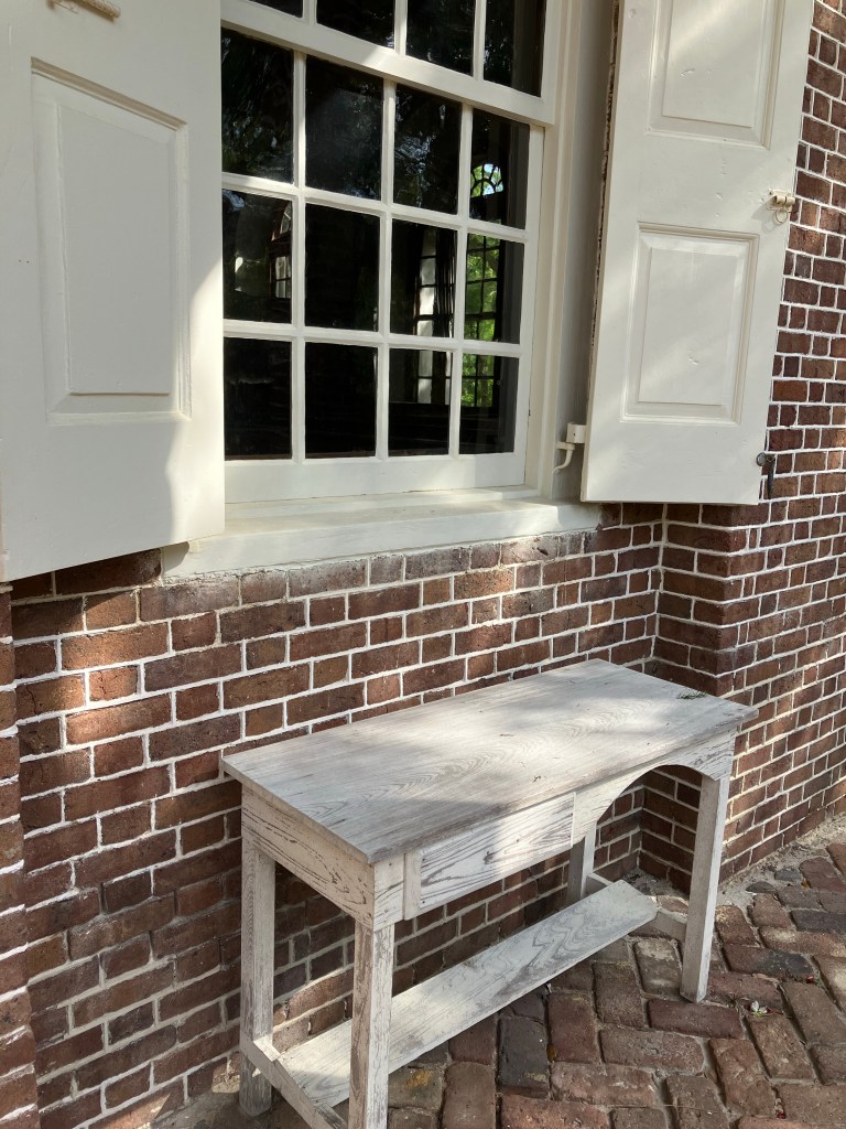 Old white table under a shuttered window on the brick porch
