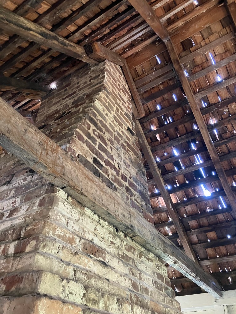 Brick chimney rising through the open rafters of an outbuilding