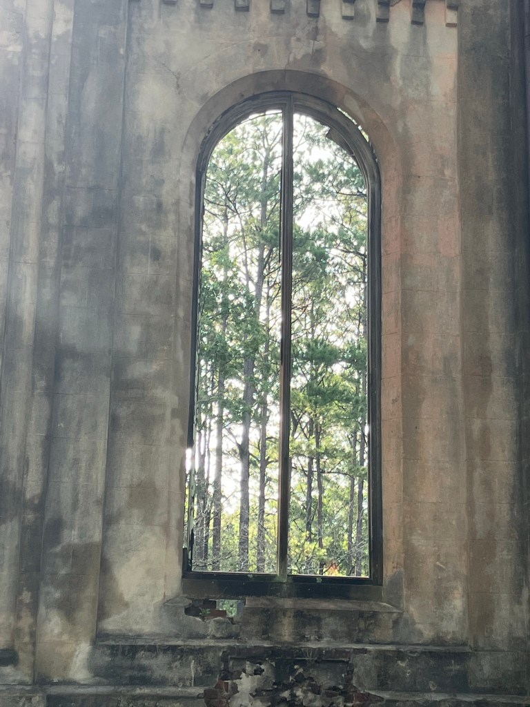 Arched window seen from inside the chapel ruins, framing green trees