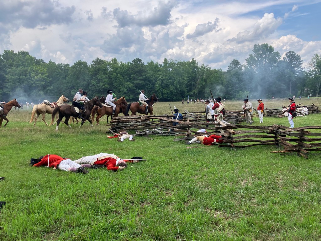 Mounted reenactors charging past fallen redcoats at Huck's Defeat
