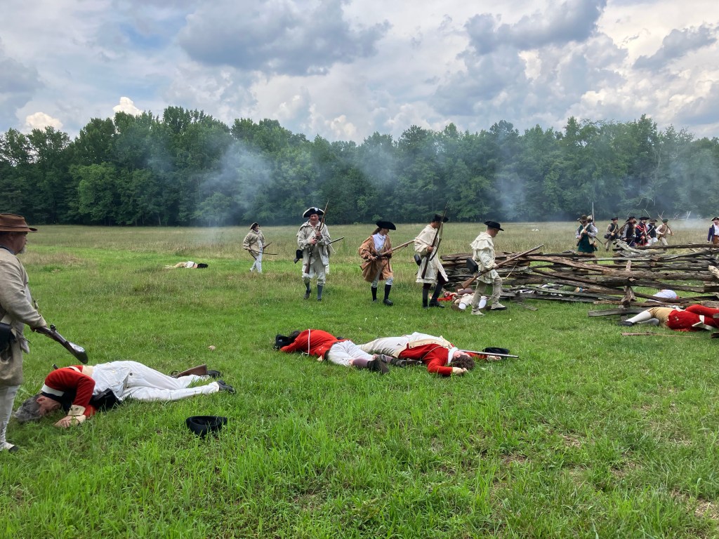 Reenactors in red coats lying in the field after a volley at Huck's Defeat