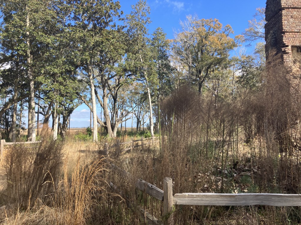 Brick chimney ruin beyond a rail fence and tall grass