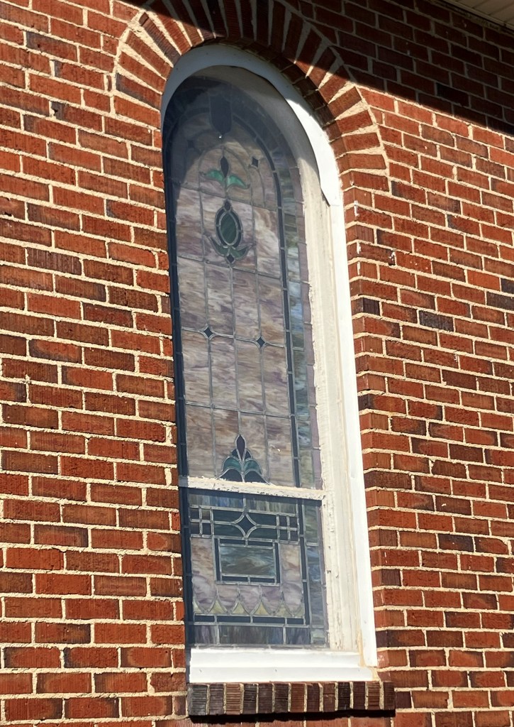 Arched stained glass window seen from outside in the brick wall of the church