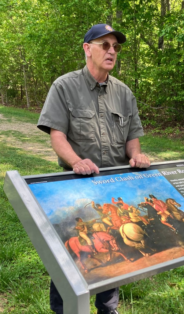 Durant Ashmore at a park sign with a painting of the cavalry fight