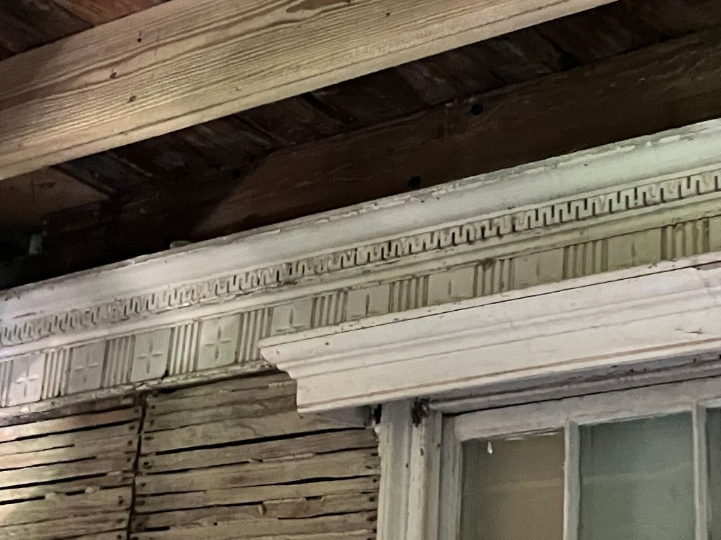 Carved molding above a window with exposed siding behind