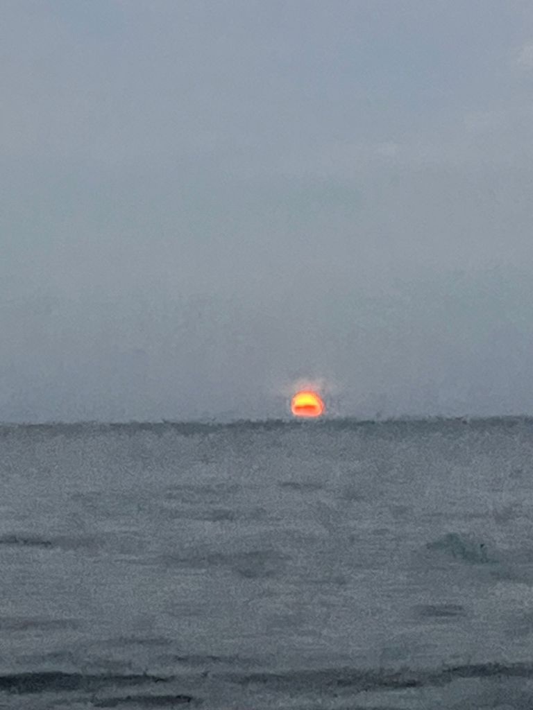 Red sun setting into the hazy water