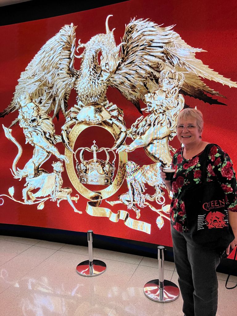 Lisa posing in front of a giant silver Queen crest on a red wall
