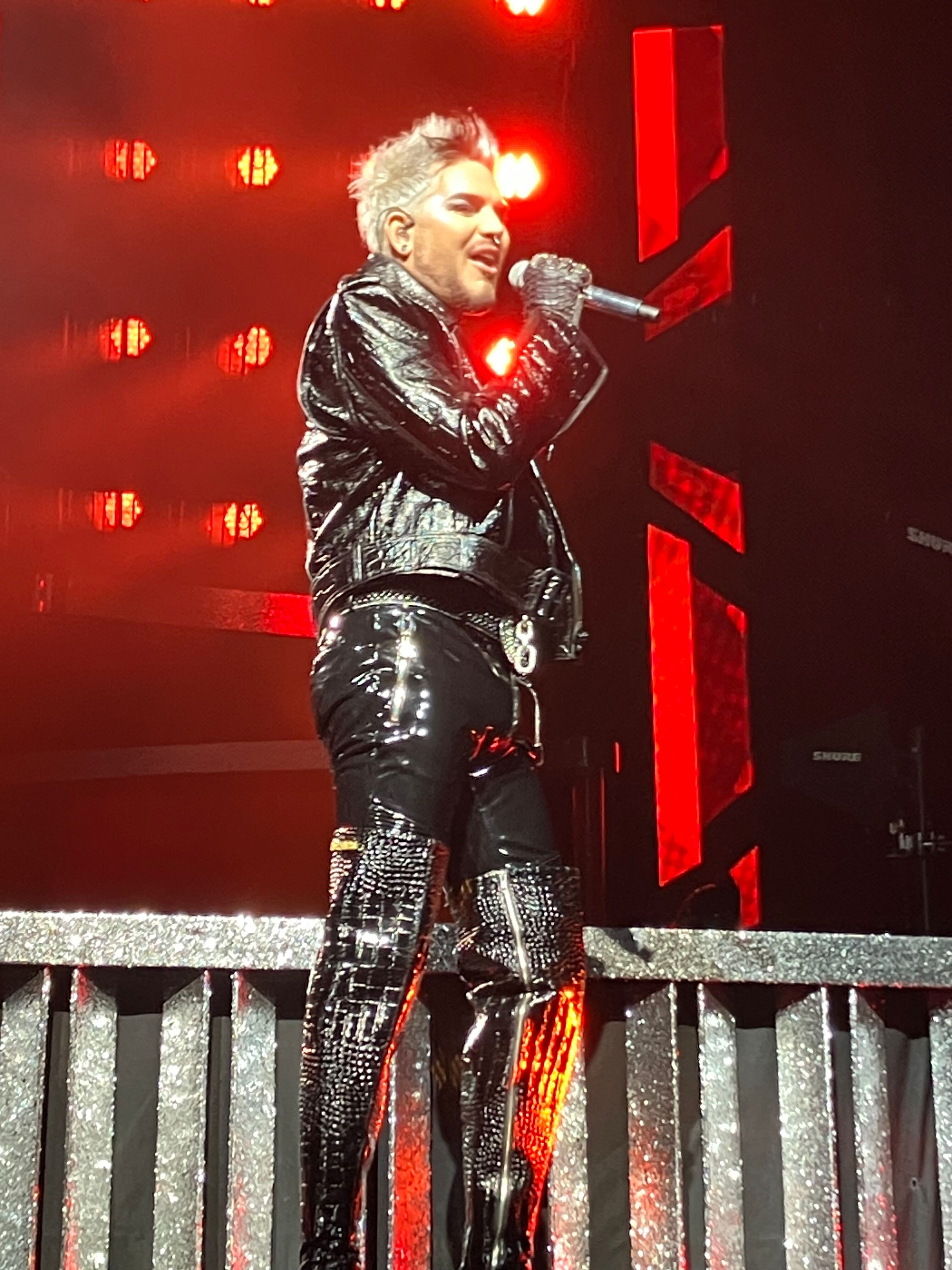 Adam Lambert singing in black leather against red lights