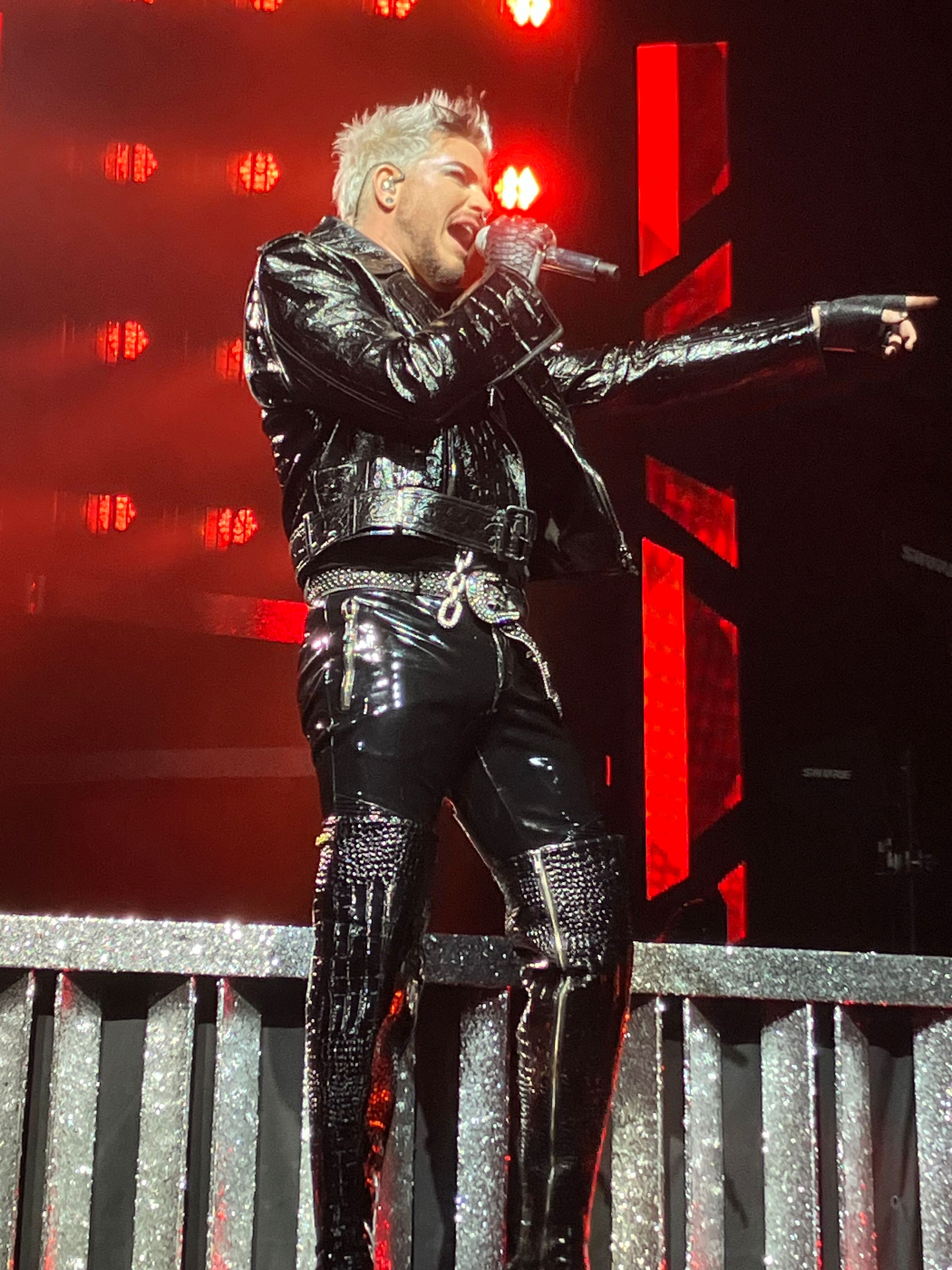 Adam Lambert singing on the catwalk with red lights behind