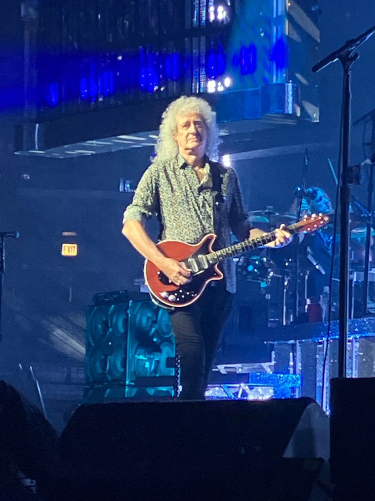 Brian May playing his red guitar under blue lights