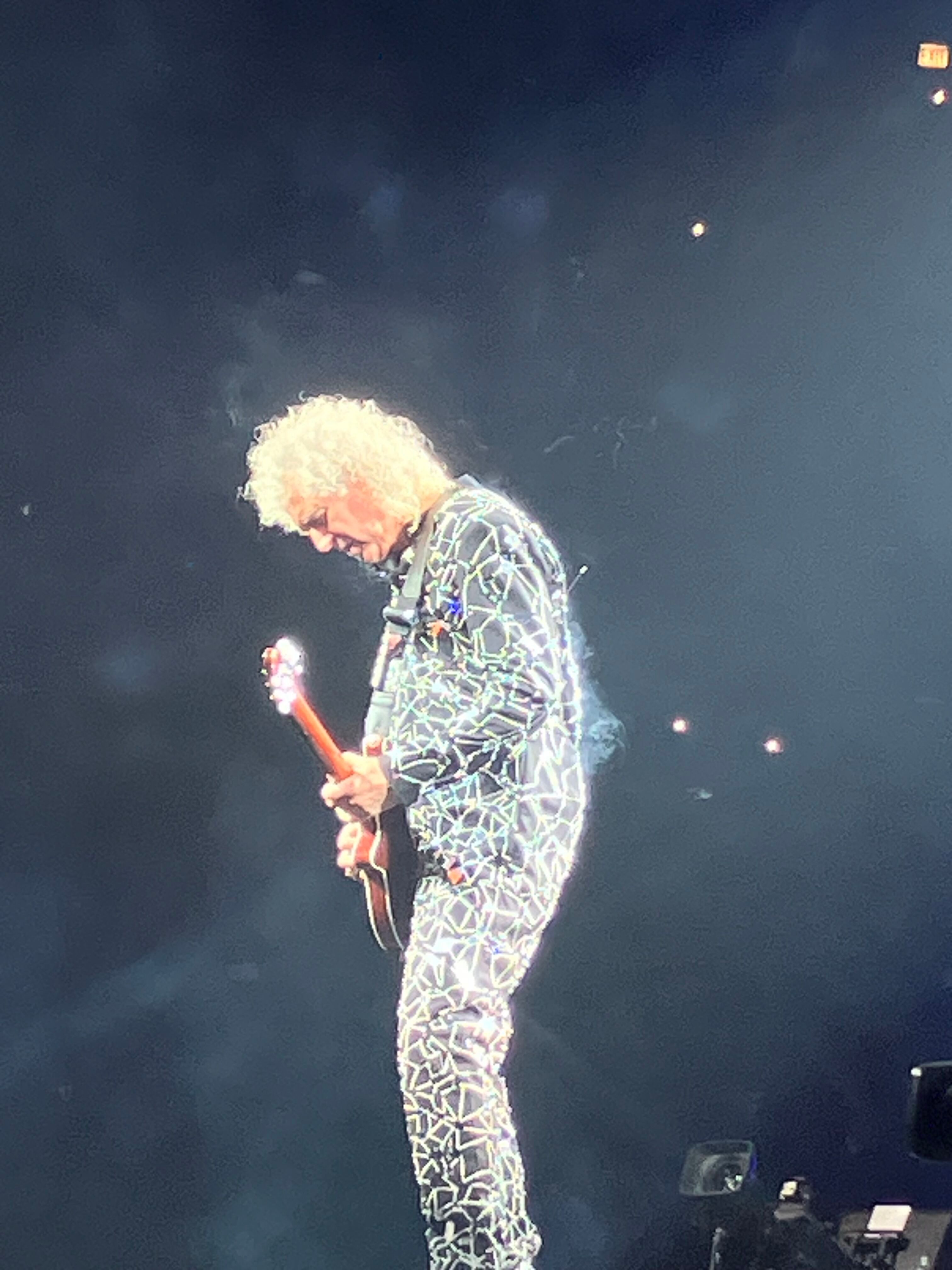 Brian May playing guitar in a sparkling jacket