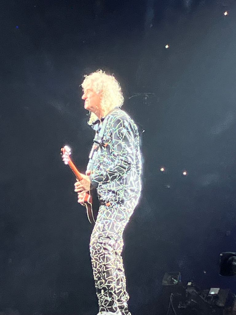 Brian May playing guitar in a sequined jacket