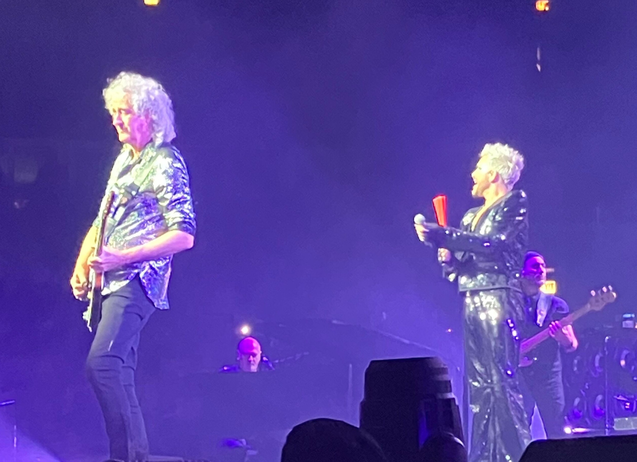 Brian May and Adam Lambert performing under blue stage lights