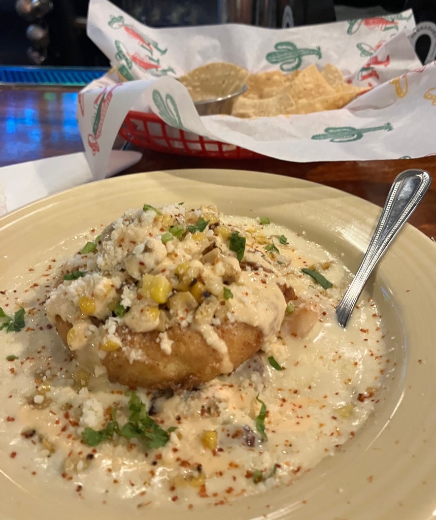 Fried dish topped with corn and herbs in a cream sauce, with chips on the side