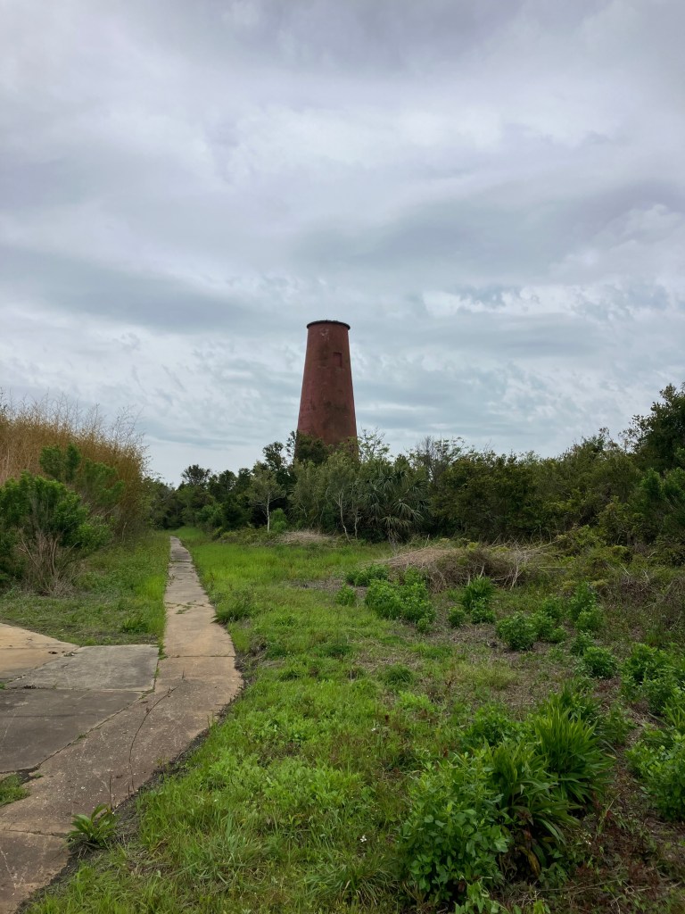The 1827 lighthouse tower beyond a concrete path and green shrubs