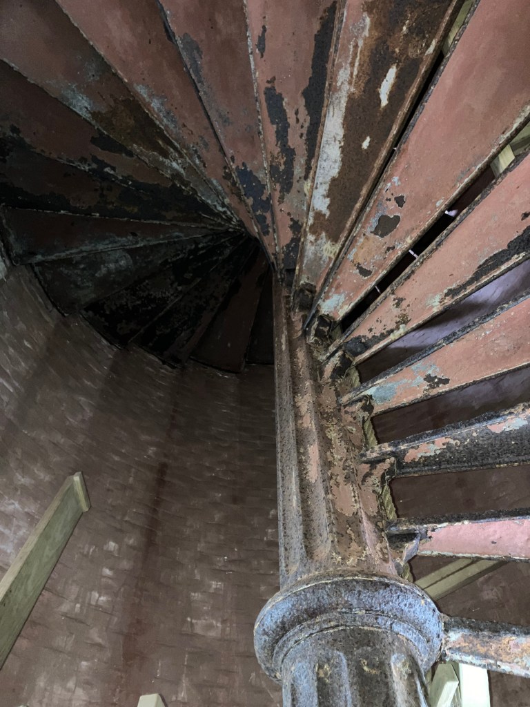 Looking up the rusted iron spiral staircase inside the lighthouse