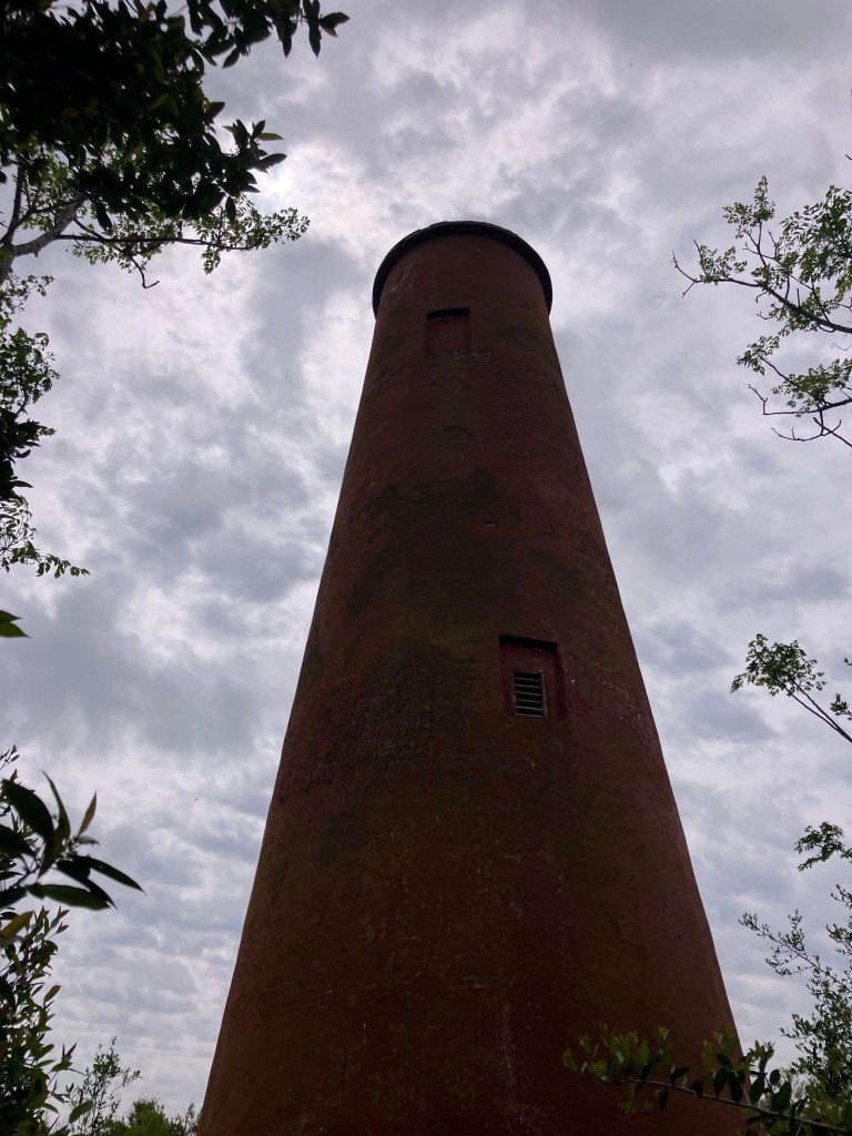 The brick 1827 lighthouse framed by trees under a cloudy sky
