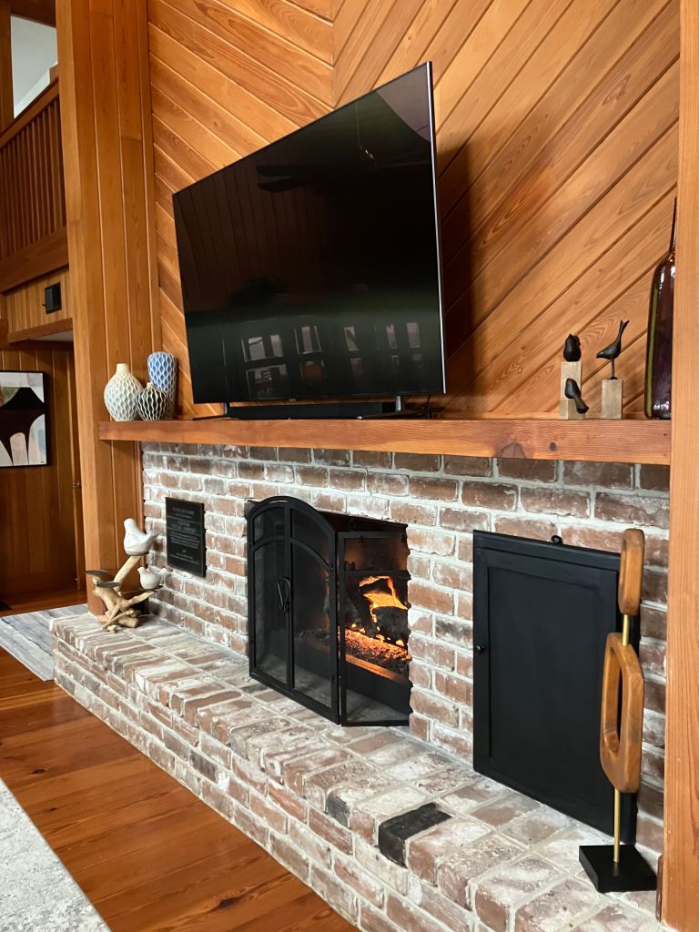Brick fireplace under a wall-mounted TV in the wood-paneled room