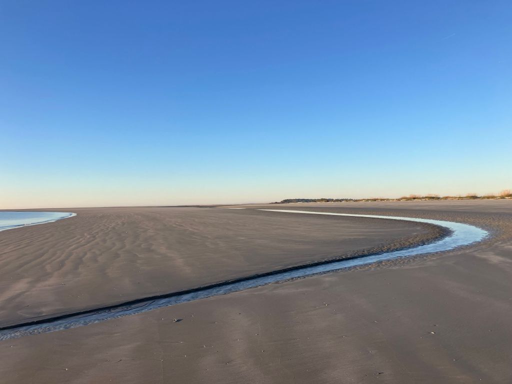 Wide sandy beach with a tidal creek winding to the sea
