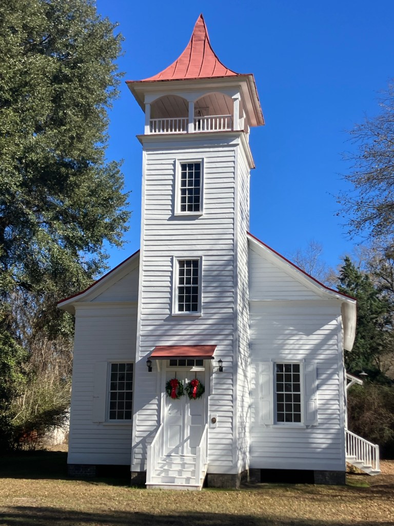 White wooden Pineville Chapel with a red-roofed bell tower and Christmas wreaths