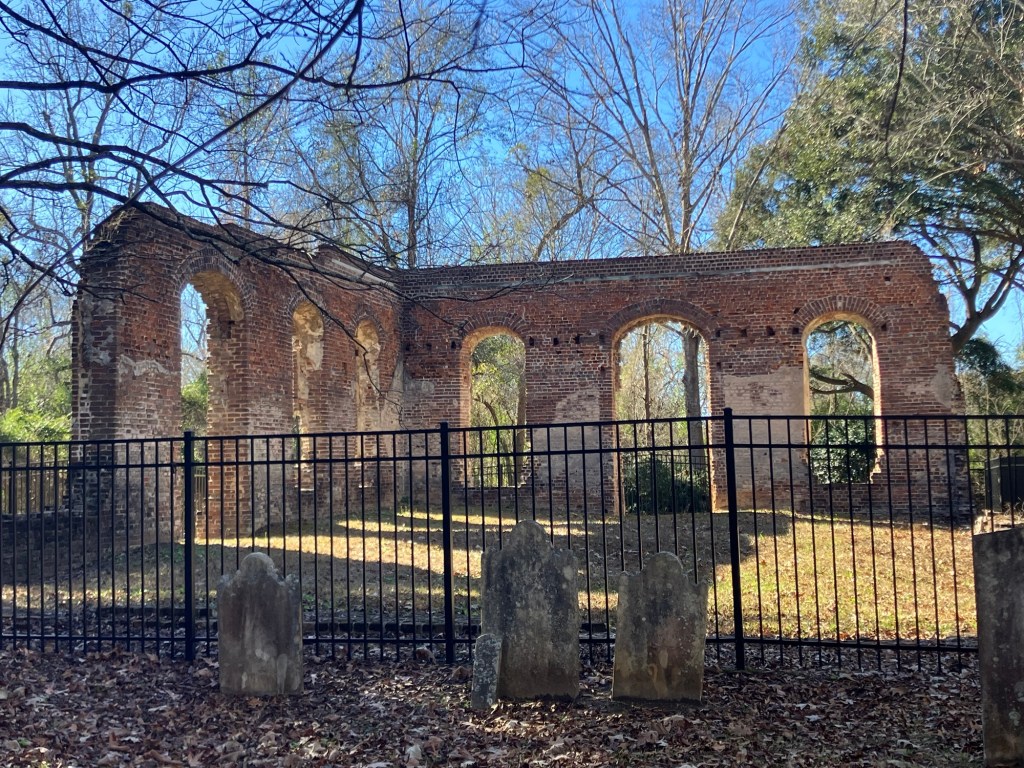 Roofless brick walls of the Biggin Church ruins behind an iron fence