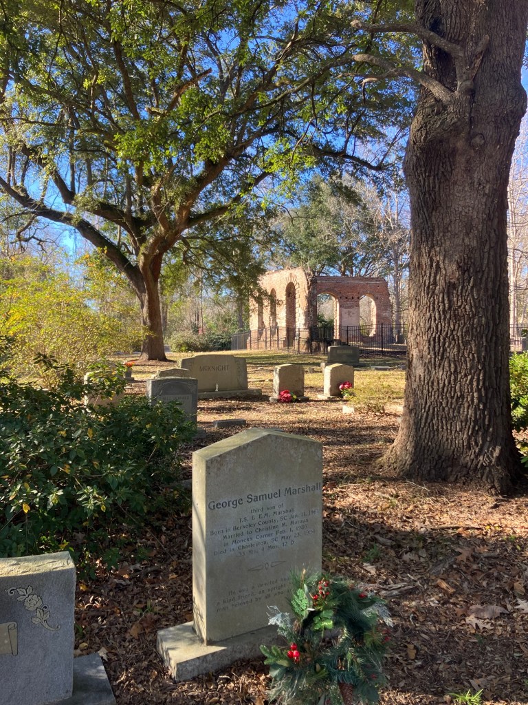 Gravestones in the churchyard with the church ruins and live oaks beyond