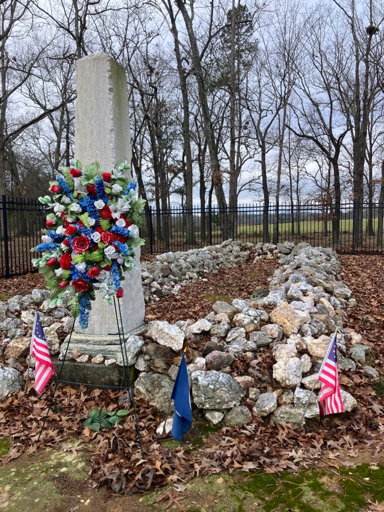 The marble marker and stone-covered mass grave at the Waxhaws battlefield with a large wreath and flags