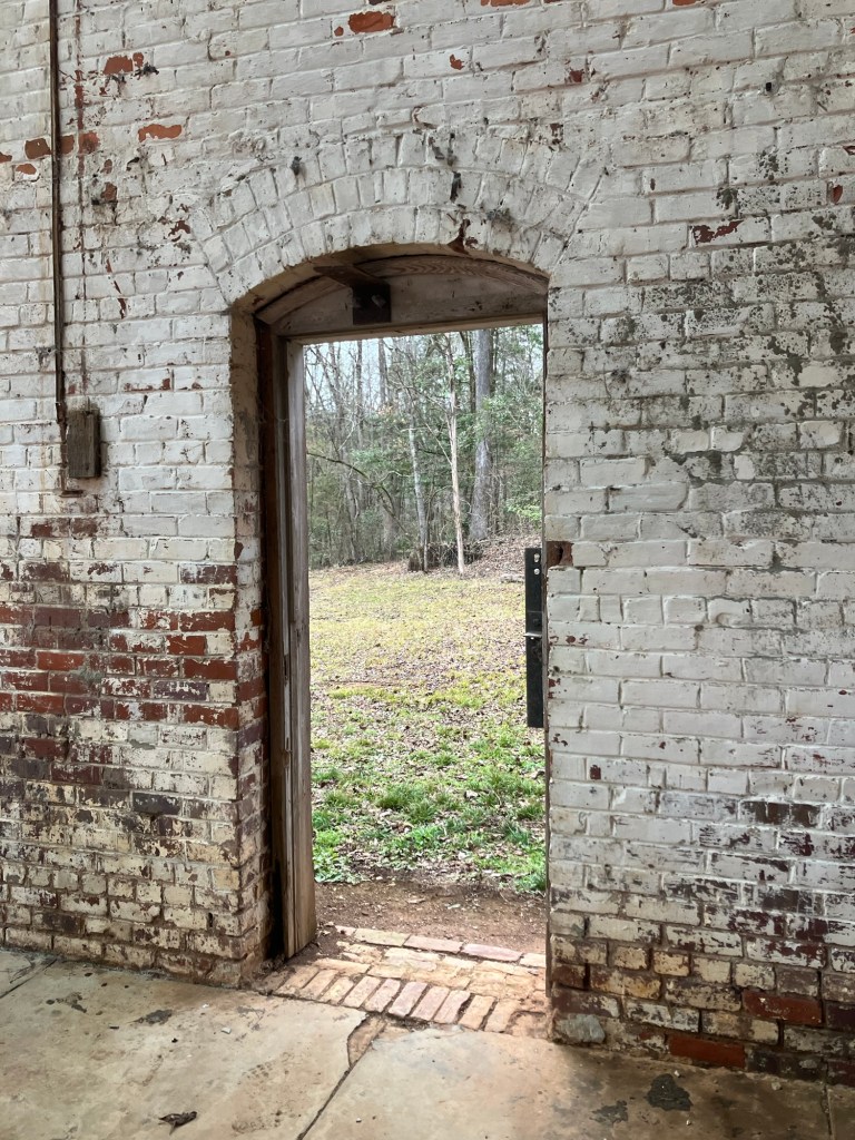Arched doorway in the whitewashed brick wall looking out to the woods