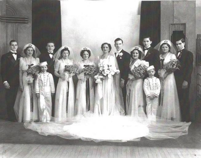 Large wedding party lined up outdoors: the bride and groom with bridesmaids in long gowns and groomsmen in dark suits