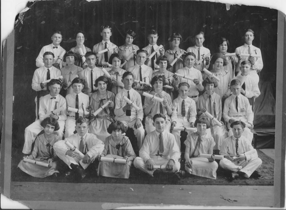 Eighth-grade graduating class of about forty boys and girls in rows, each holding a rolled diploma