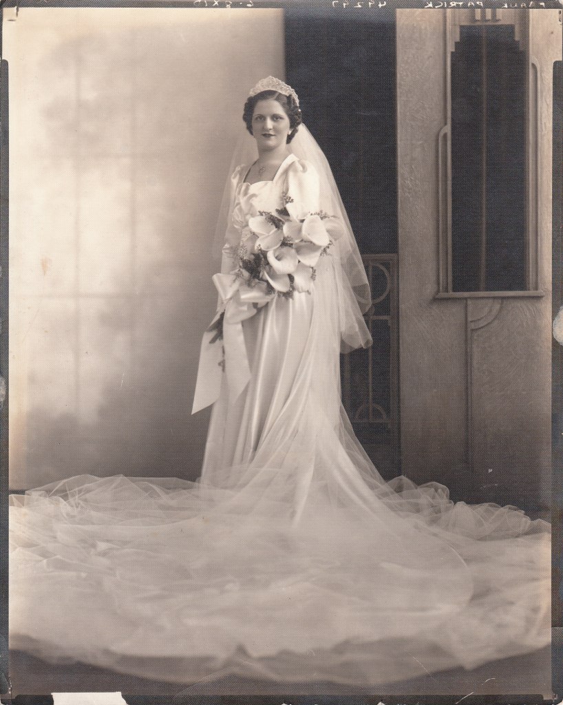 Camille Leonetti in her wedding gown and long veil, holding a bouquet, standing in a doorway