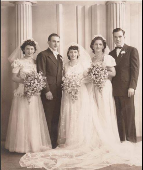 Studio wedding portrait of five people: the bride and groom with two bridesmaids and a groomsman, the women holding large bouquets